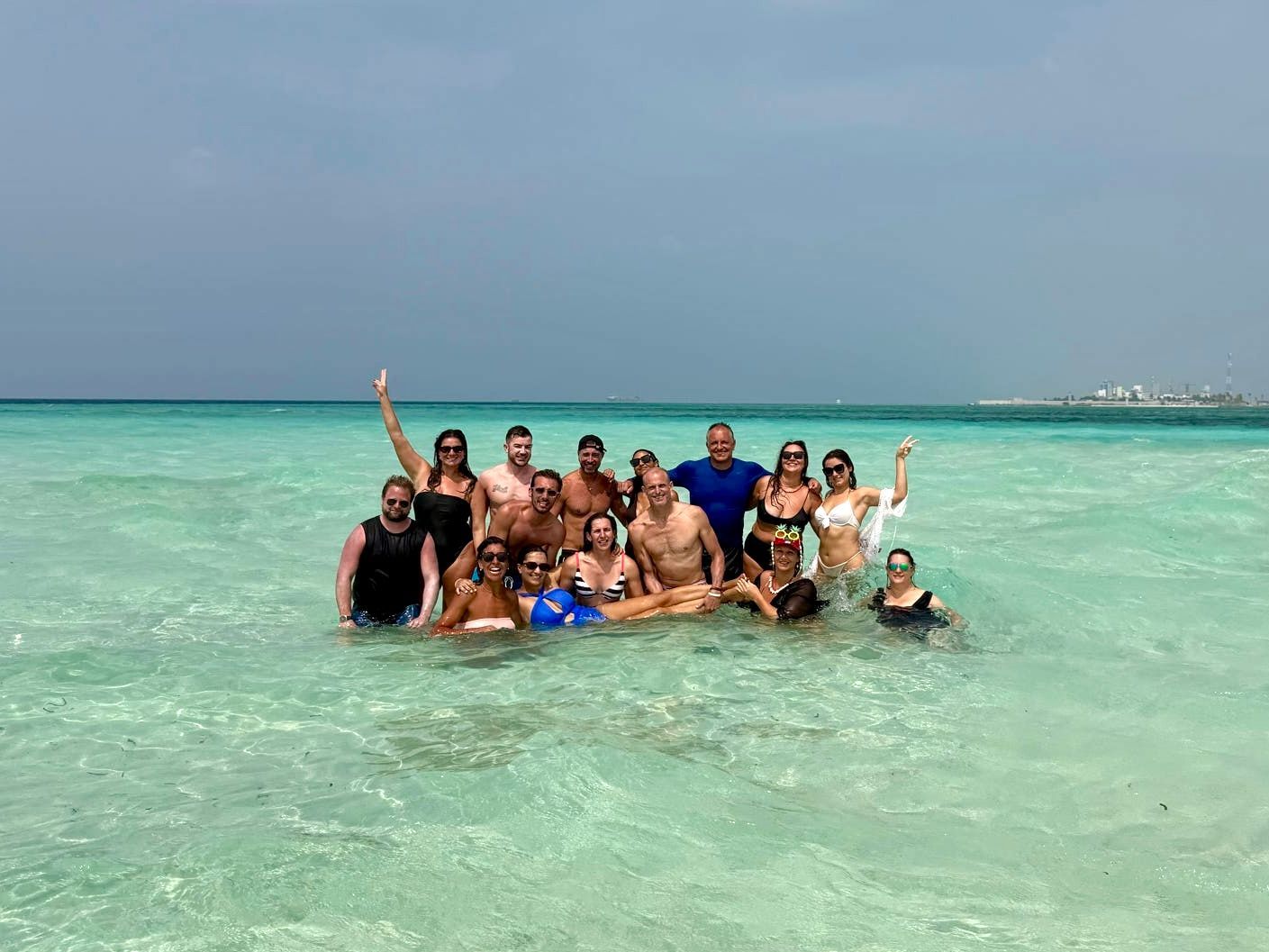 Un groupe WeRoad prend la pose pour une photo, debout dans l'eau claire et turquoise de l'océan, sous un ciel gris.