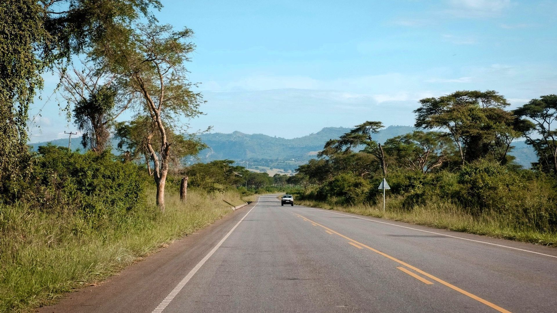 Ein weißer SUV fährt auf einer asphaltierten Straße durch eine ländliche Landschaft mit üppig grünen Bäumen und Hügeln in der Ferne.