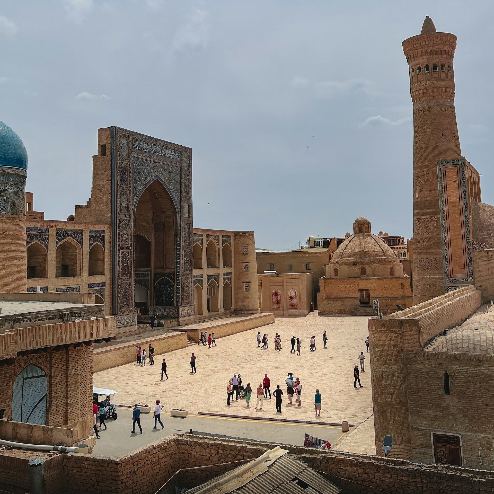 Una vista dall'alto di persone che camminano in una piazza storica circondata da edifici in mattoni decorati, un minareto e cupole.