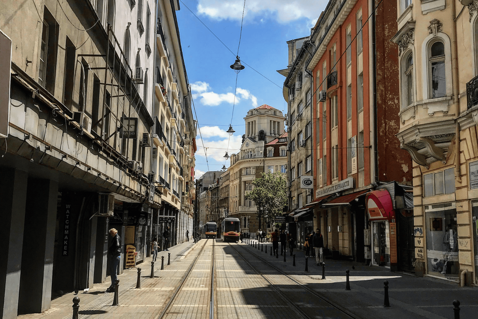 Un tranvía recorre una calle de la ciudad con vías entre edificios altos y clásicos bajo un cielo azul con nubes.