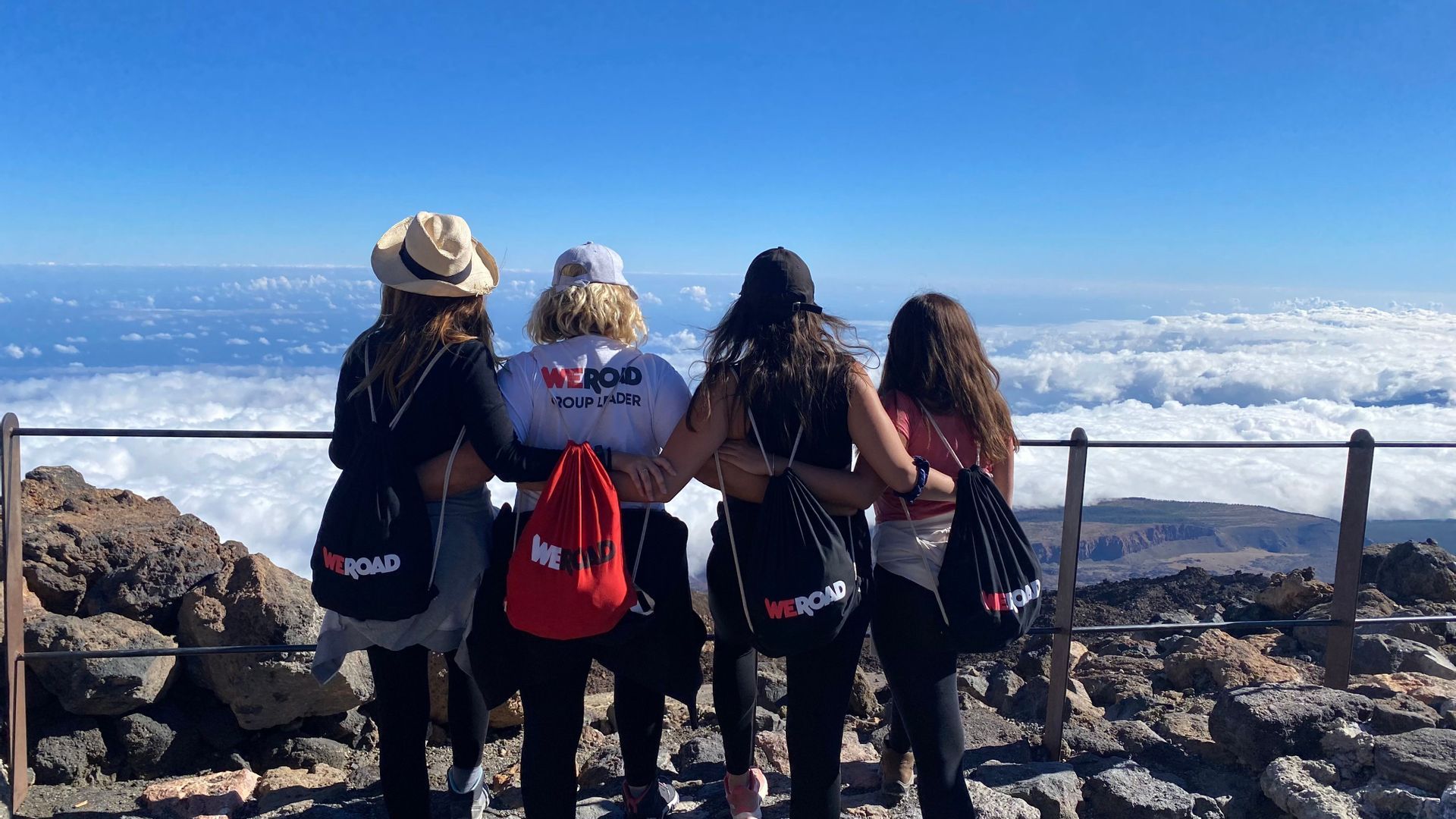 Un voyage de groupe WeRoad de quatre femmes, bras dessus bras dessous, contemplant une mer de nuages depuis le sommet d'une montagne.