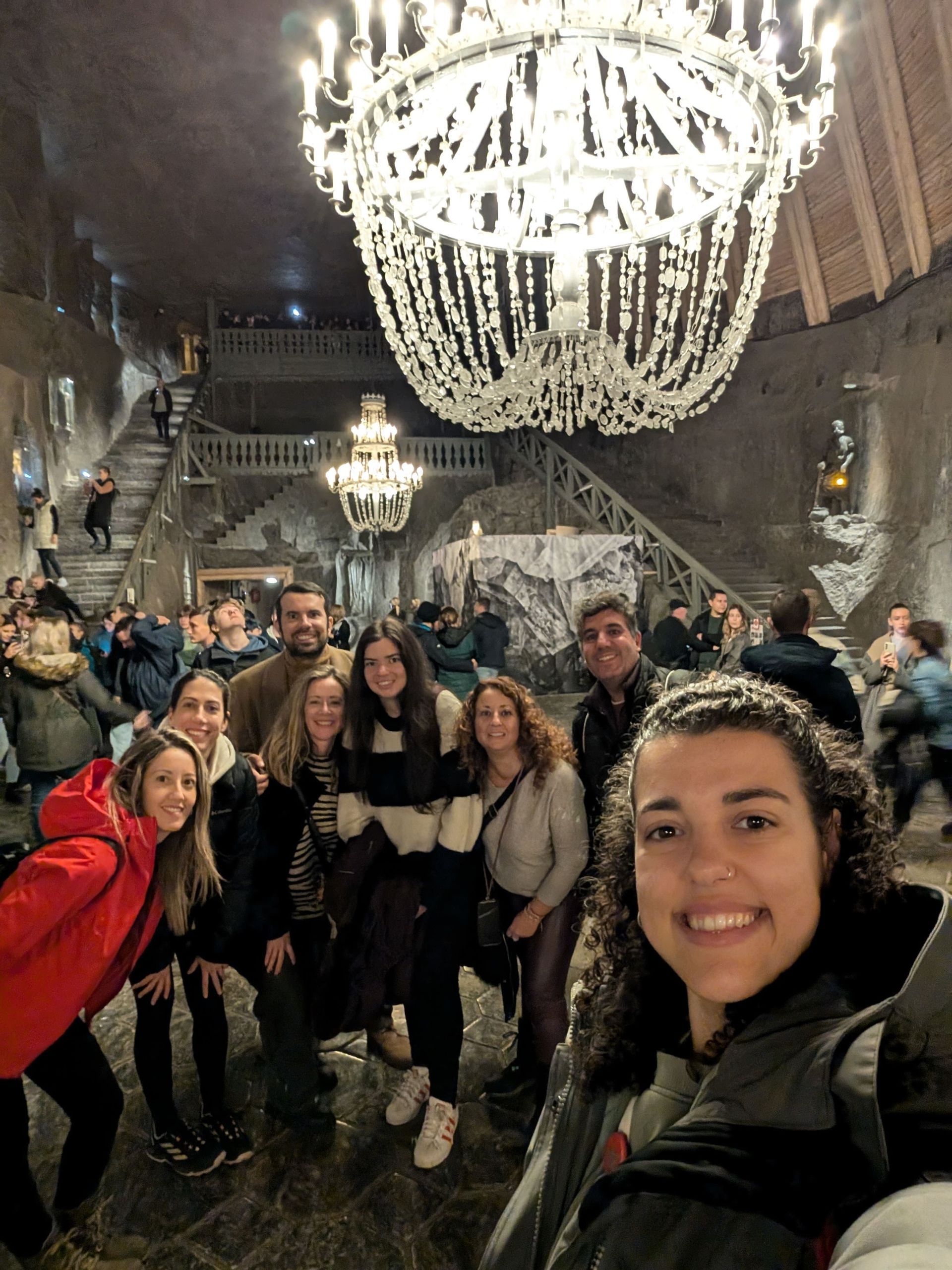 Un viaje en grupo de WeRoad se toma una selfie dentro de una gran caverna subterránea decorada con ornamentadas lámparas de araña de cristal.