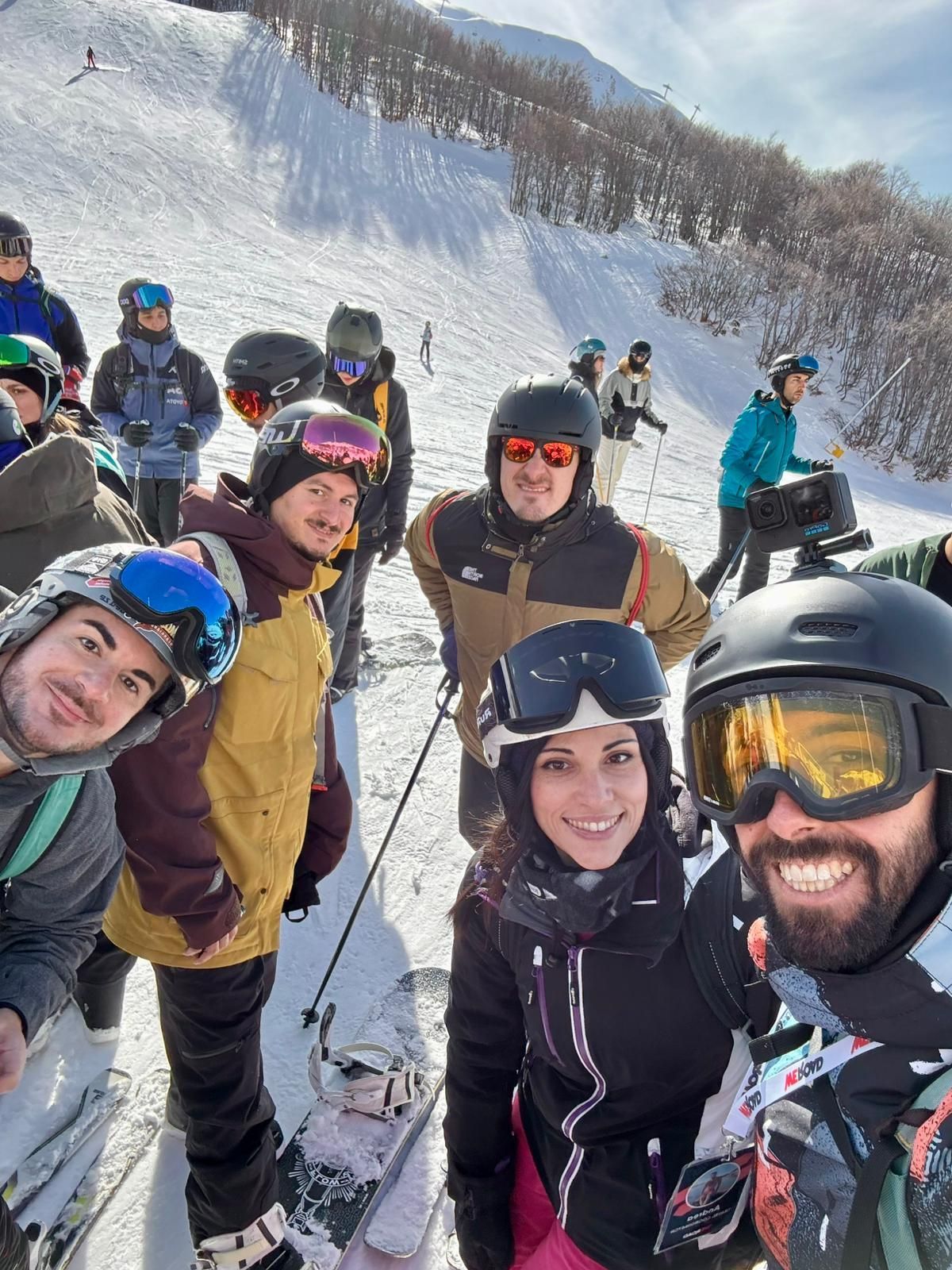 A WeRoad group trip in ski gear smiling for a selfie on a snowy mountain slope.
