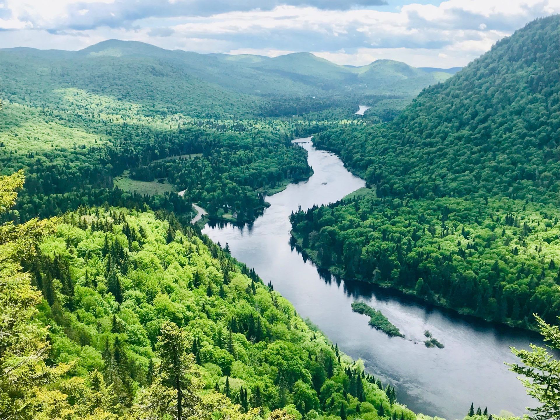 Vue aérienne d'une large rivière serpentant à travers une vaste vallée couverte de forêts verdoyantes et de collines vallonnées.
