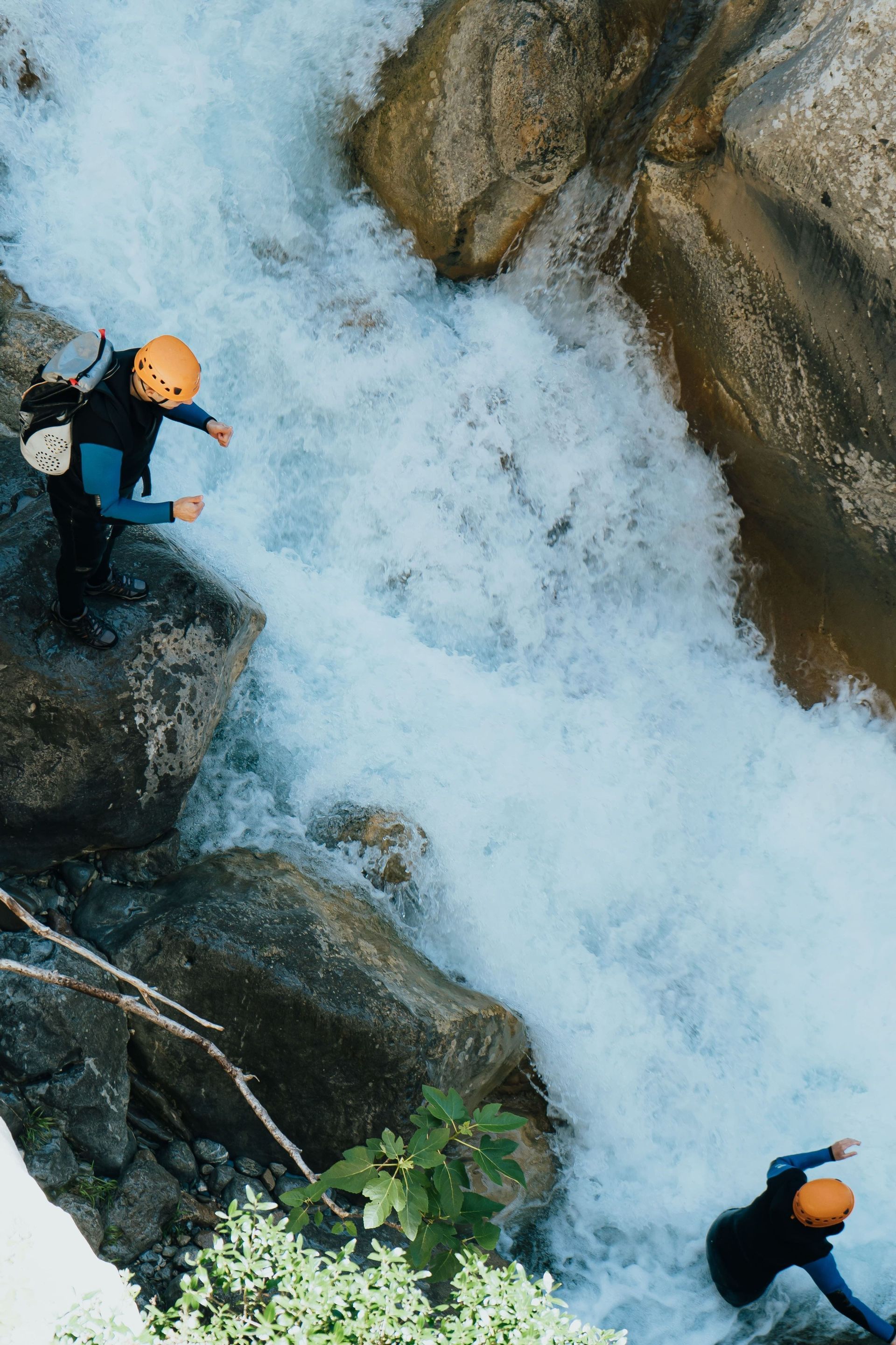 Zwei WeRoad-Reisende beim Canyoning an einem rauschenden Wasserfall zwischen steilen Canyonwänden, aus der Vogelperspektive.