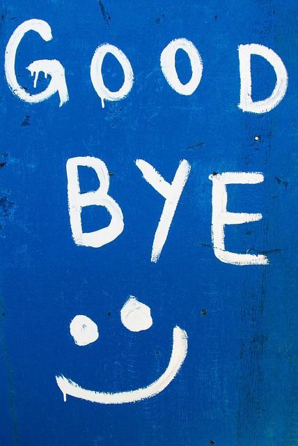 Die Worte 'GOOD BYE' und ein Smiley, handgemalt in Weiß mit tropfender Farbe auf einer hellblauen Holzoberfläche.