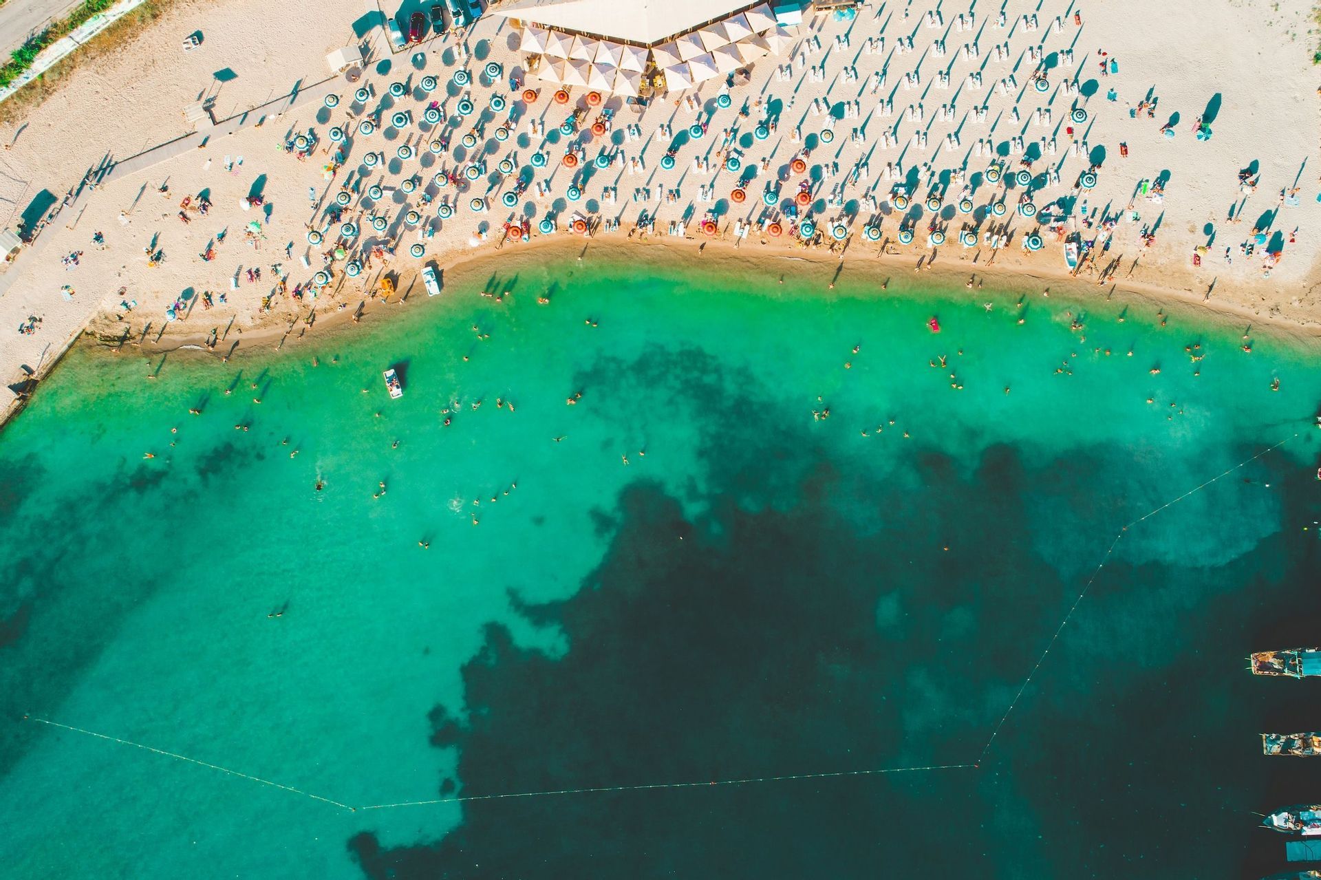 Una vista aerea di una spiaggia affollata con persone che nuotano in acqua turchese e si rilassano sotto ombrelloni colorati sulla sabbia.