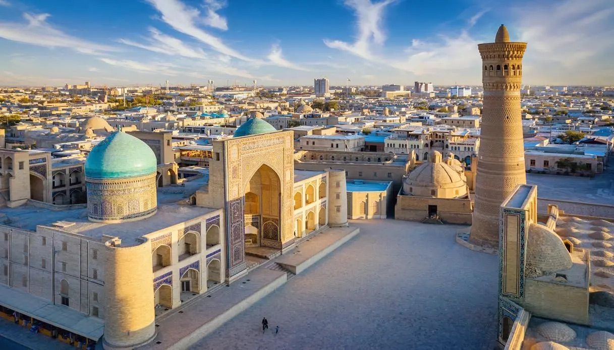 Vue aérienne d'une place historique avec un dôme turquoise et un haut minaret au lever du soleil.