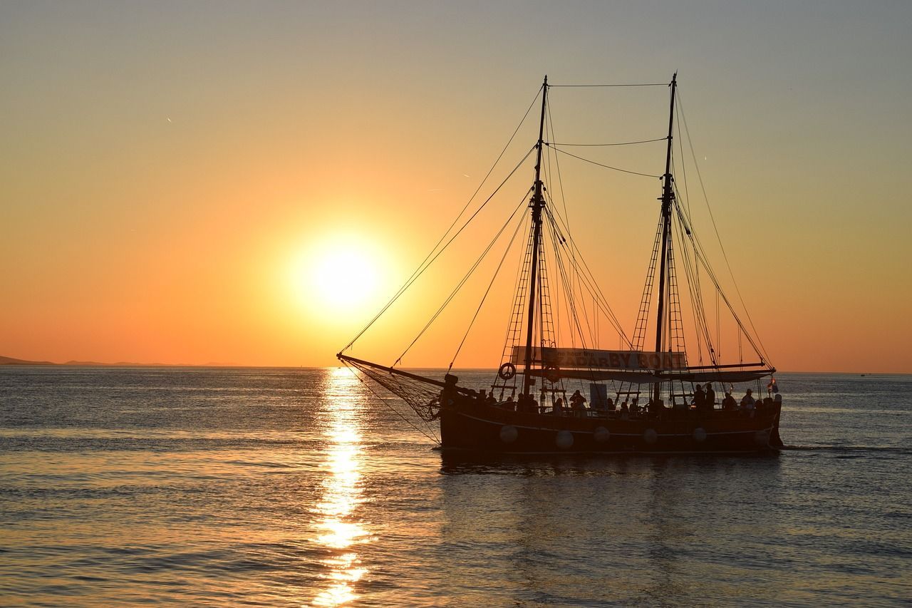 Eine silhouettierte Galeone mit einer WeRoad Gruppenreise an Bord segelt bei einem leuchtend orangefarbenen Sonnenuntergang über den Ozean.