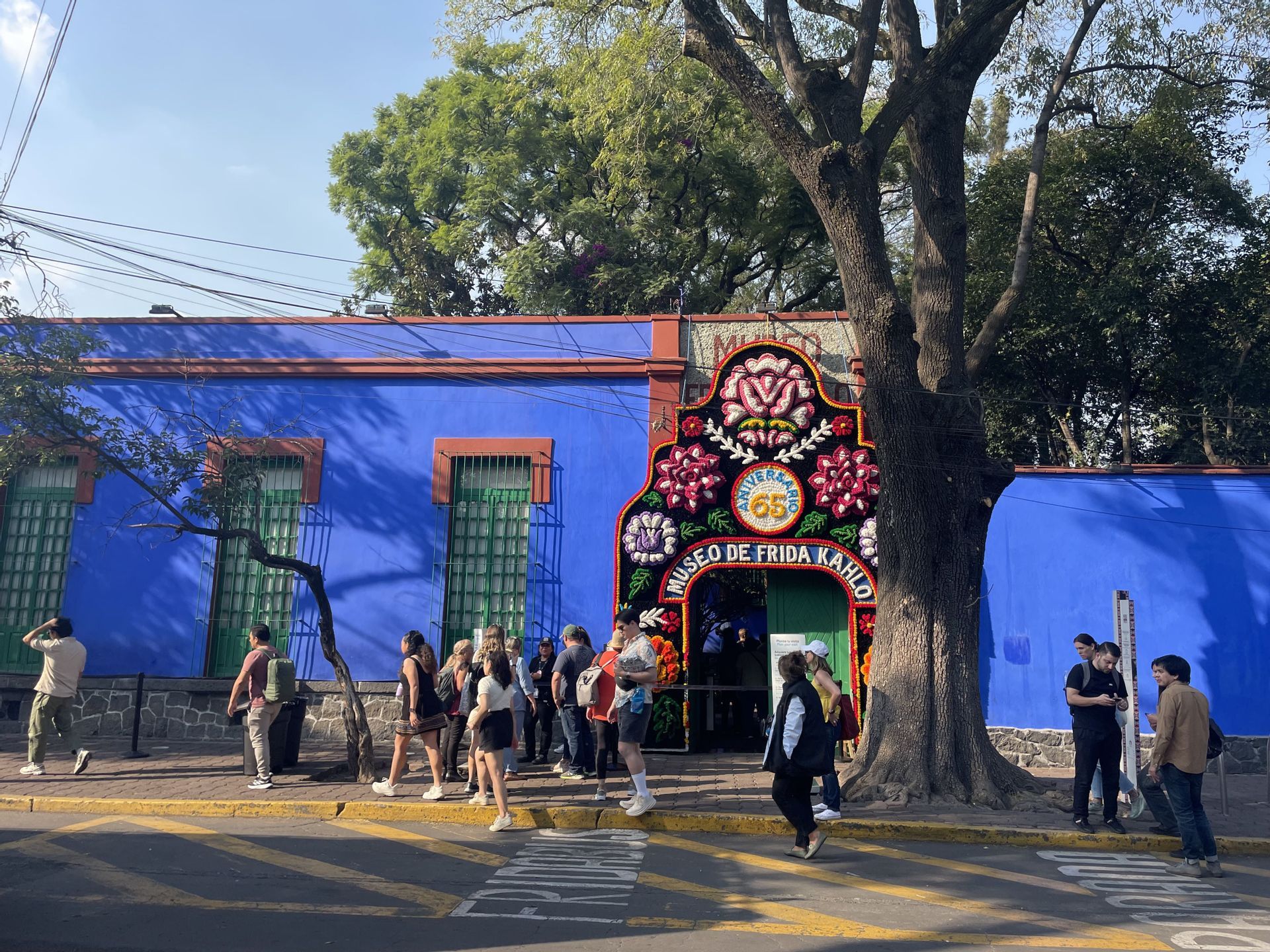 Un groupe WeRoad fait la queue sur un trottoir face à l'entrée d'un bâtiment bleu éclatant orné d'une grande arche florale.
