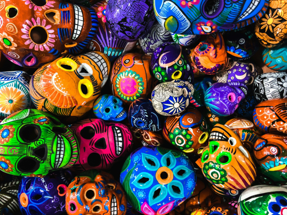 Vue plongeante rapprochée de nombreux crânes Calavera colorés, peints à la main, avec des motifs floraux et géométriques complexes.