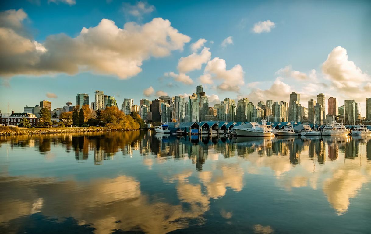 Un horizonte urbano moderno y barcos atracados reflejándose a la perfección en las tranquilas aguas de un puerto bajo un cielo parcialmente nublado.