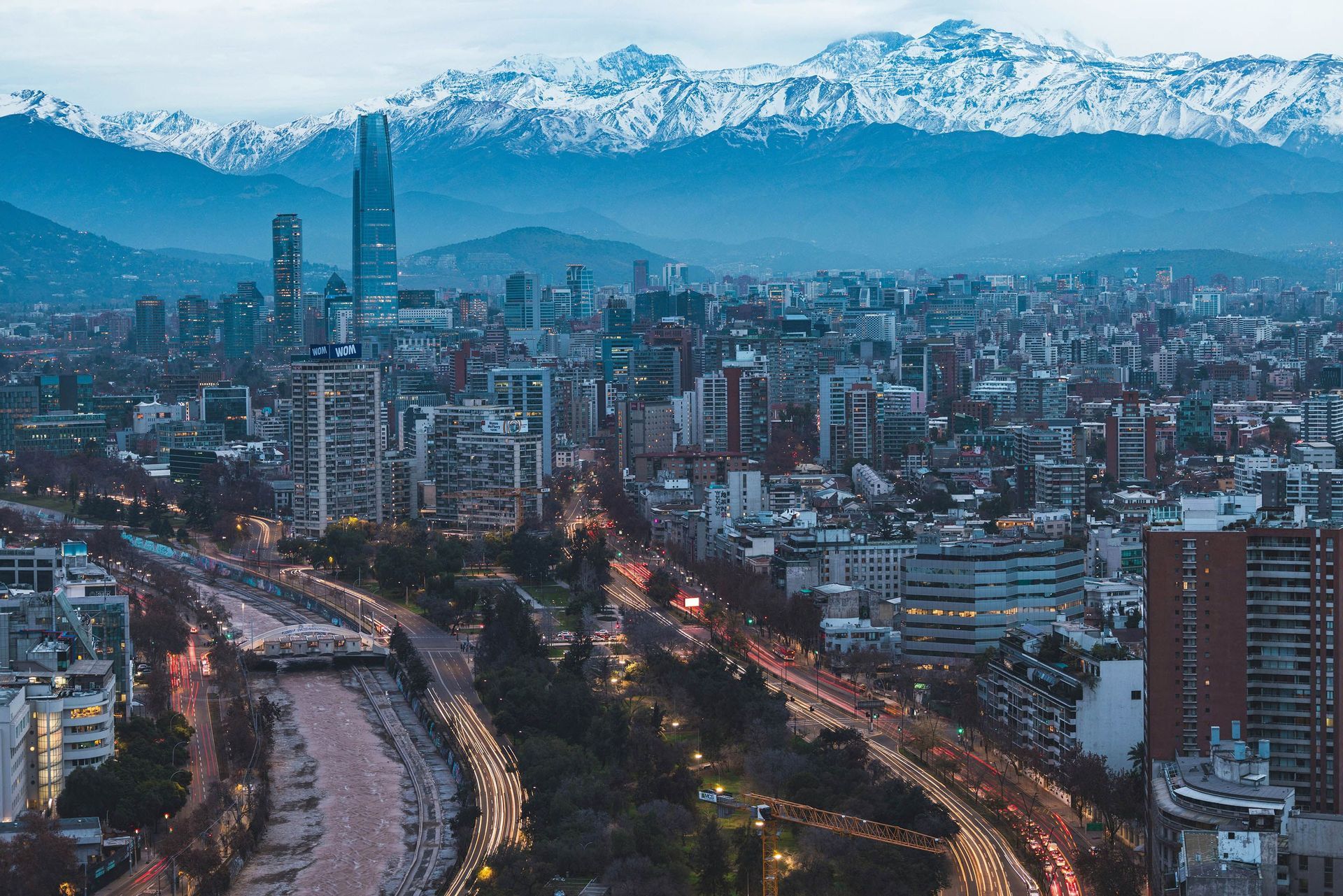 Un denso panorama urbano con edifici illuminati al tramonto, sullo sfondo di grandi montagne innevate.