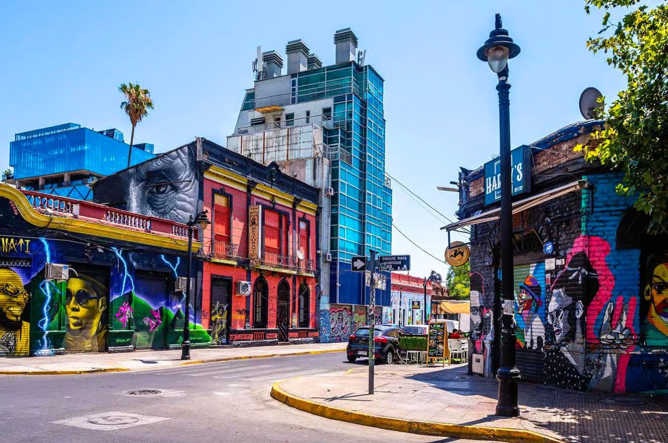 Un angolo di strada cittadino soleggiato con graffiti colorati sui palazzi, accanto a un moderno grattacielo di vetro.