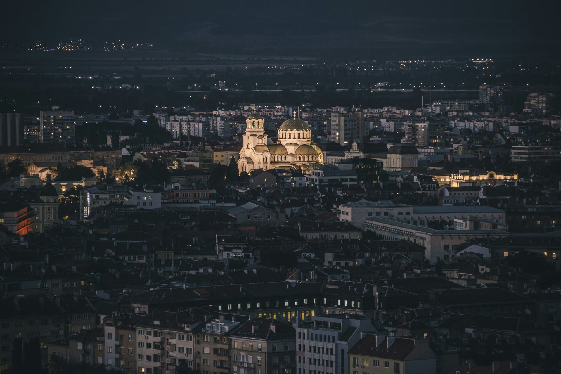 Une cathédrale illuminée aux multiples dômes dorés trône au centre d'un paysage urbain dense la nuit.