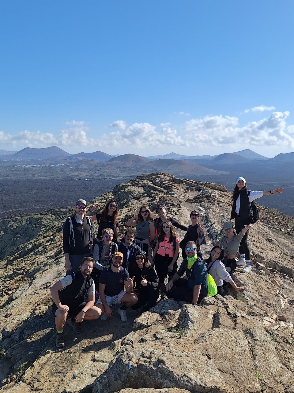 Un viaggio di gruppo WeRoad in posa per una foto su una cresta rocciosa di montagna, con un paesaggio vulcanico sullo sfondo.