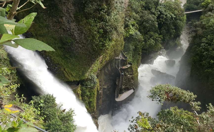 Una vista dall'alto di una grande cascata che si getta in una gola verde lussureggiante, con una scala in pietra tortuosa sulla parete rocciosa.