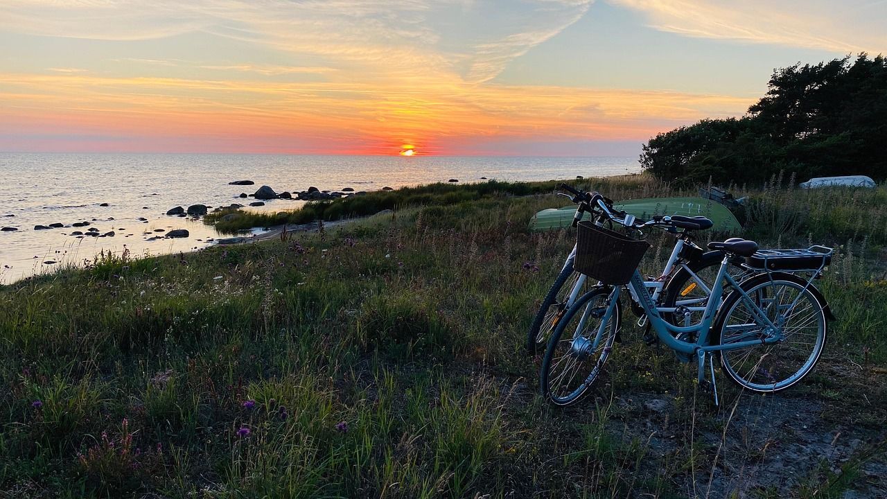 Zwei Fahrräder stehen an einer grasbewachsenen Küste mit Blick auf den Ozean, während die Sonne am Horizont untergeht.
