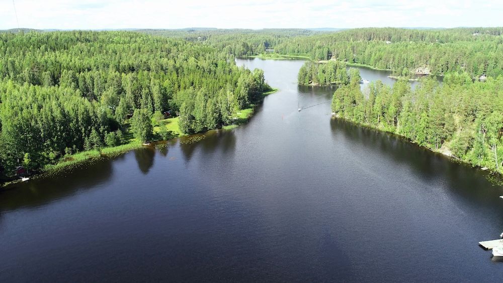Una vista aerea di un lago blu scuro che si snoda attraverso una vasta e fitta foresta verde, con una piccola barca che naviga in lontananza.