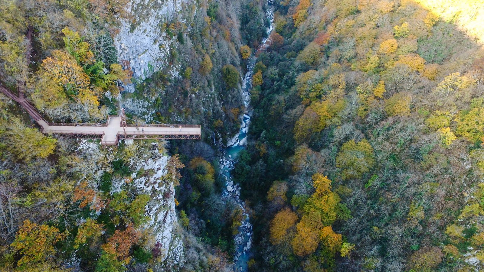 Vue aérienne d'une plateforme d'observation en forme de croix surplombant un canyon profond avec une rivière et des forêts automnales.