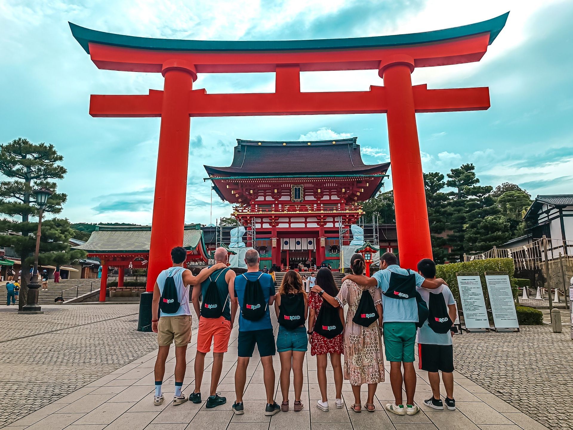 Un gruppo WeRoad in posa, di schiena alla fotocamera, ammira un tempio giapponese attraverso un grande torii rosso.