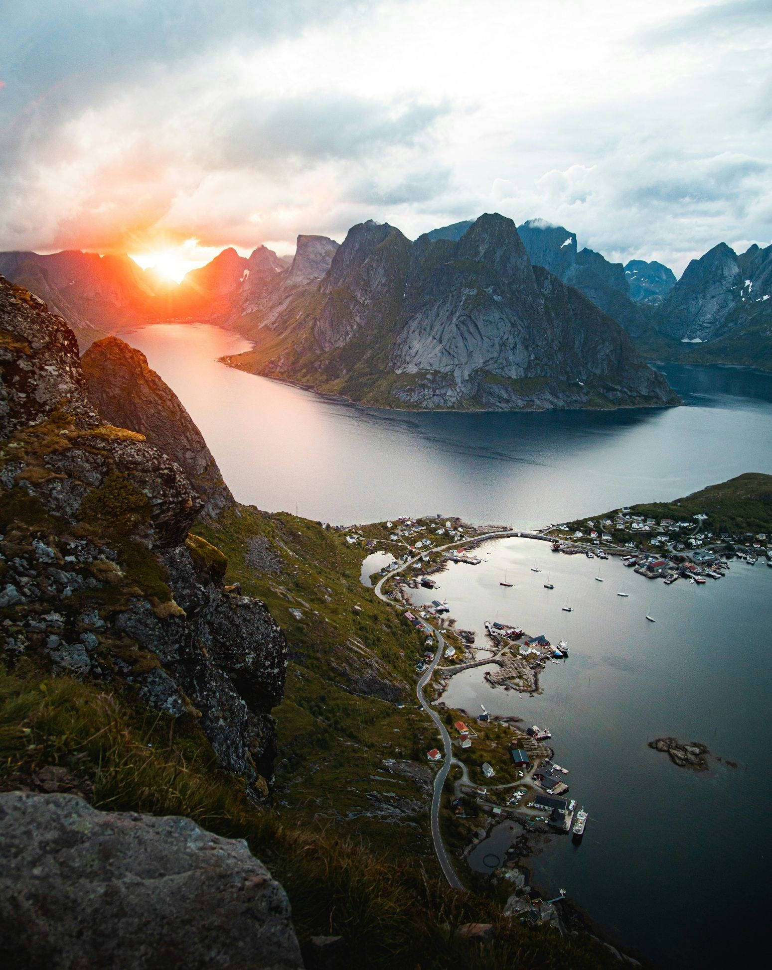Veduta panoramica di un fiordo e di un borgo costiero incastonato tra ripide montagne al tramonto vibrante.