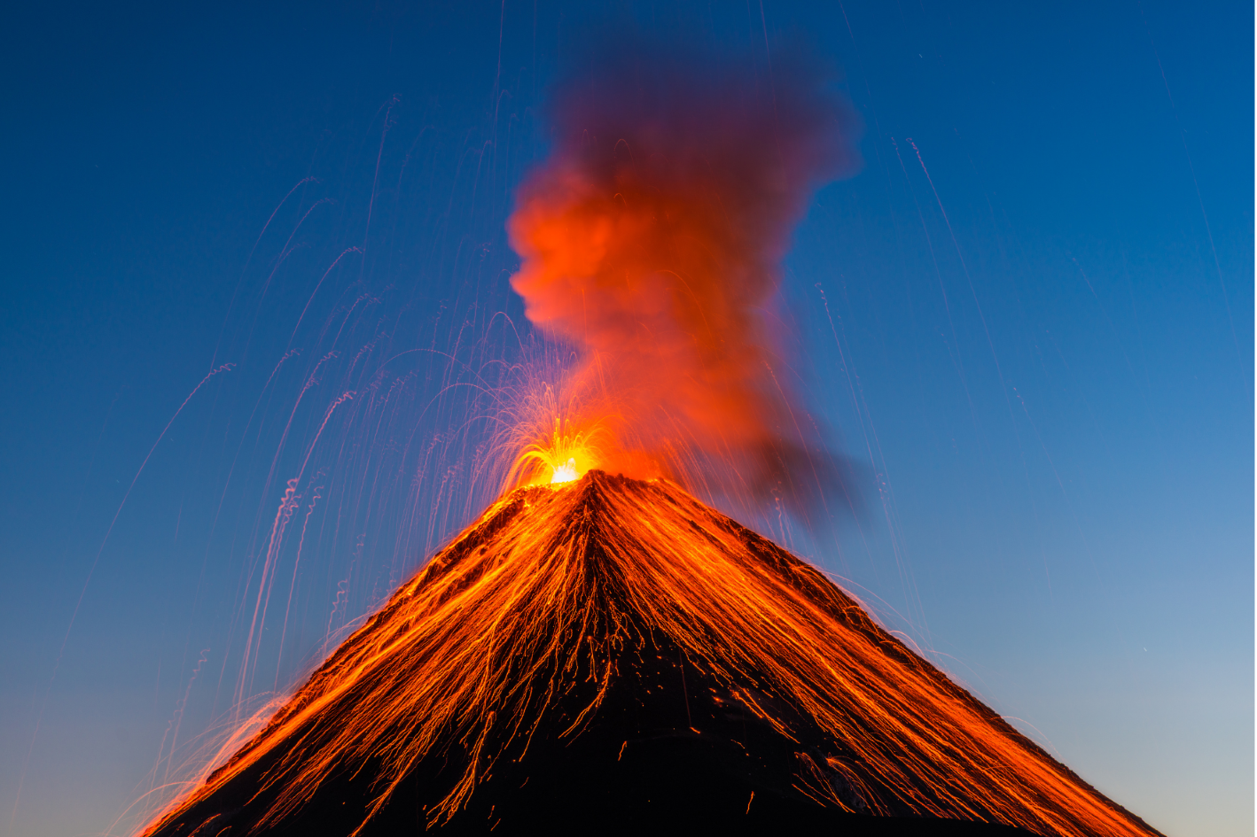 Geschmolzene Lava speit aus dem Gipfel eines ausbrechenden Vulkans und fließt in hellen Strömen dessen Hänge unter blauem Himmel hinab.