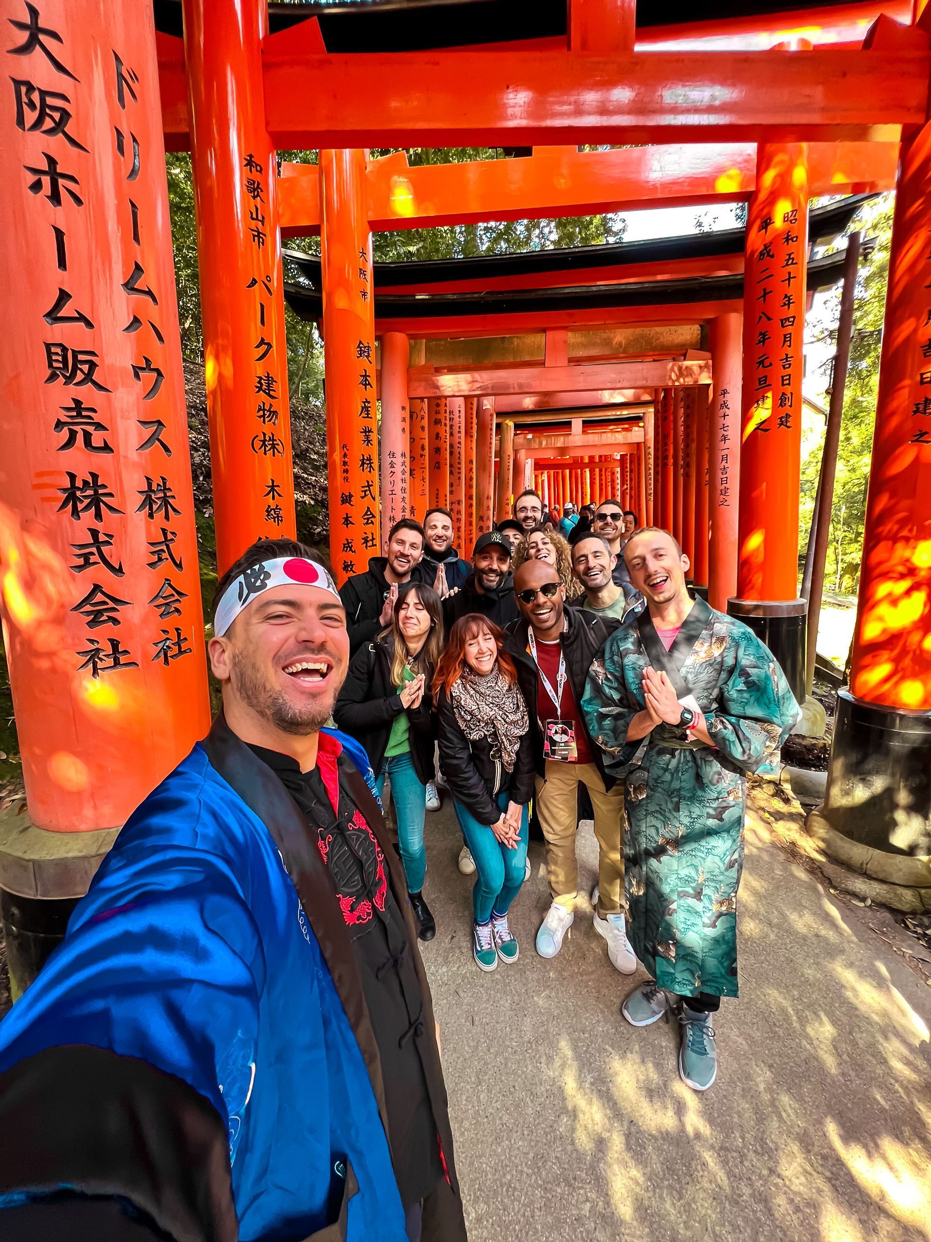 Un uomo in tunica blu si fa un selfie con un gruppo WeRoad, tutti sorridenti sotto un tunnel di torii rossi giapponesi.