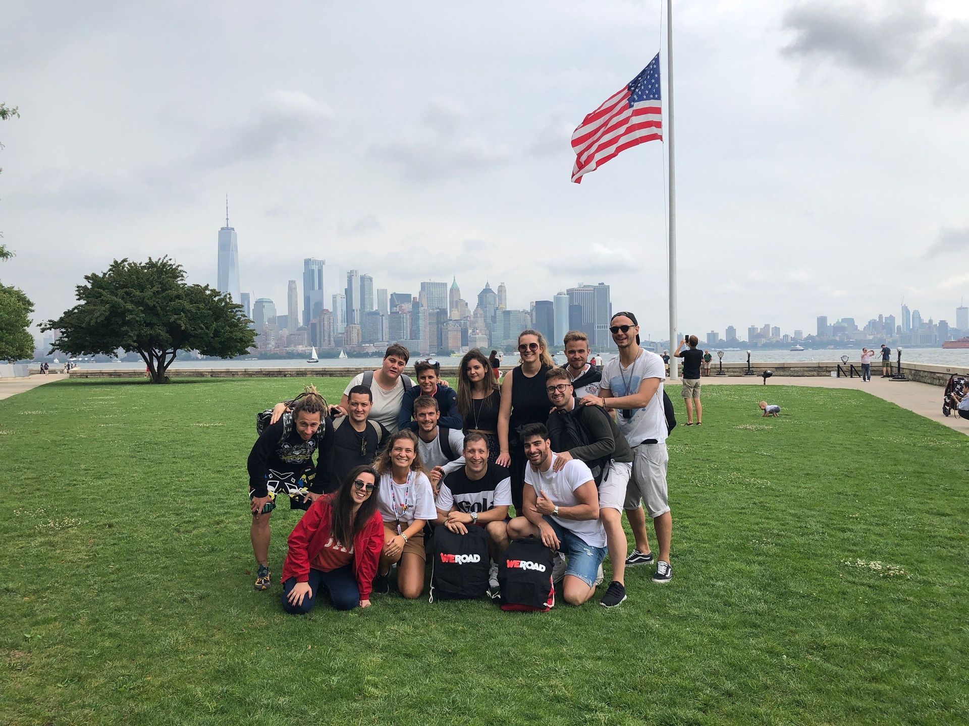 Un gruppo WeRoad in posa per una foto su un prato erboso con una bandiera americana e uno skyline cittadino sullo sfondo.