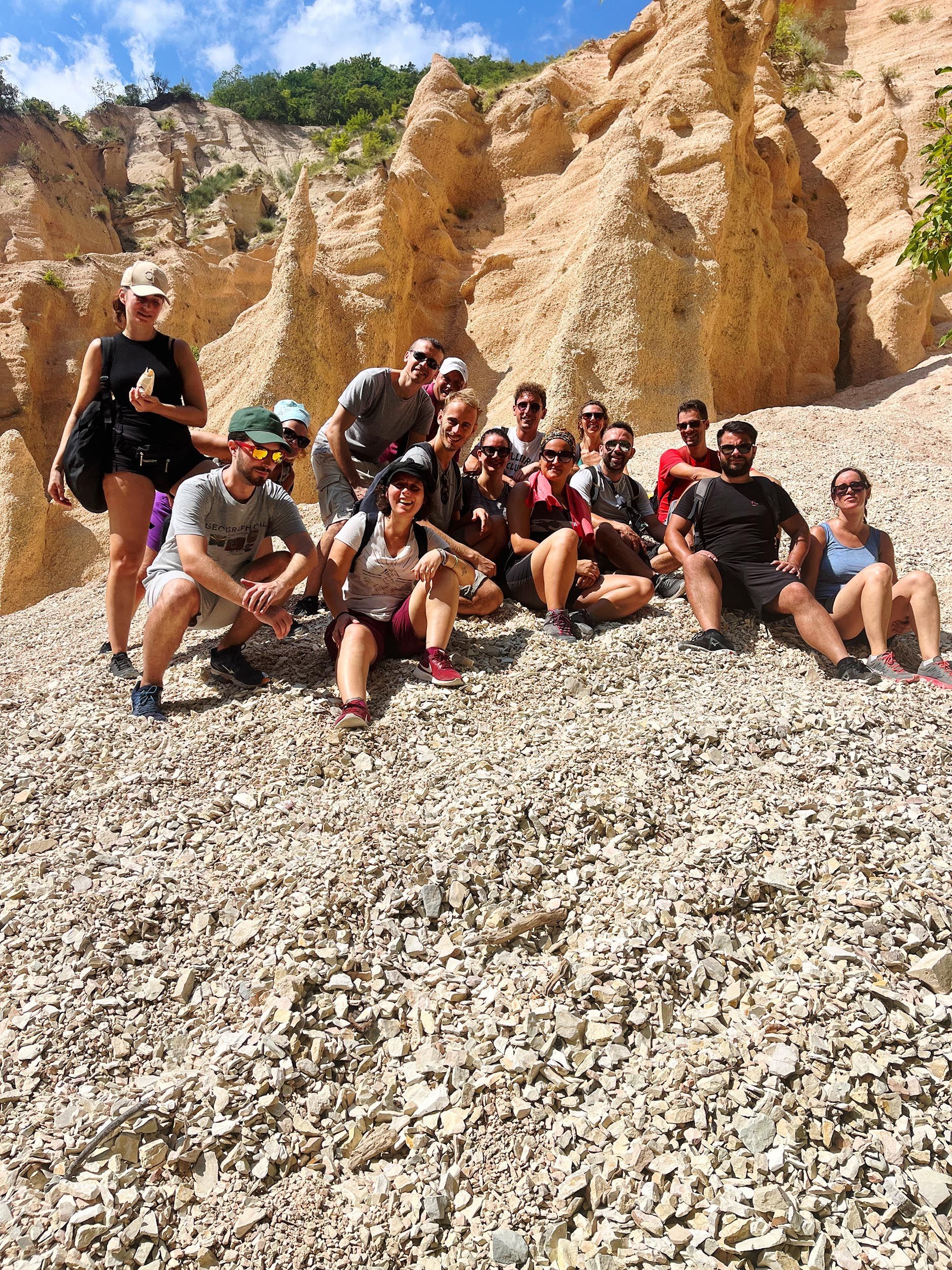 Un viaggio di gruppo WeRoad in posa per una foto su un pendio ghiaioso, con grandi formazioni rocciose erose sullo sfondo sotto un cielo blu.