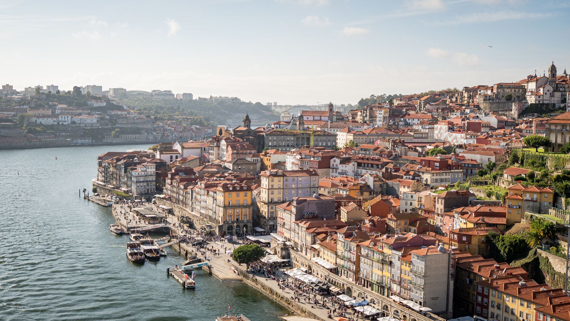 Blick von oben auf eine Stadt mit bunten Häusern und Terrakottadächern, die an einem Hang an einem breiten Fluss liegt.