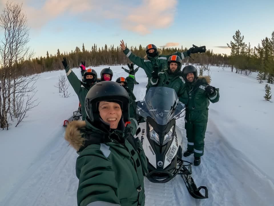Un viaje en grupo de WeRoad con equipo de invierno, haciéndose un selfie con una moto de nieve en un paisaje nevado.