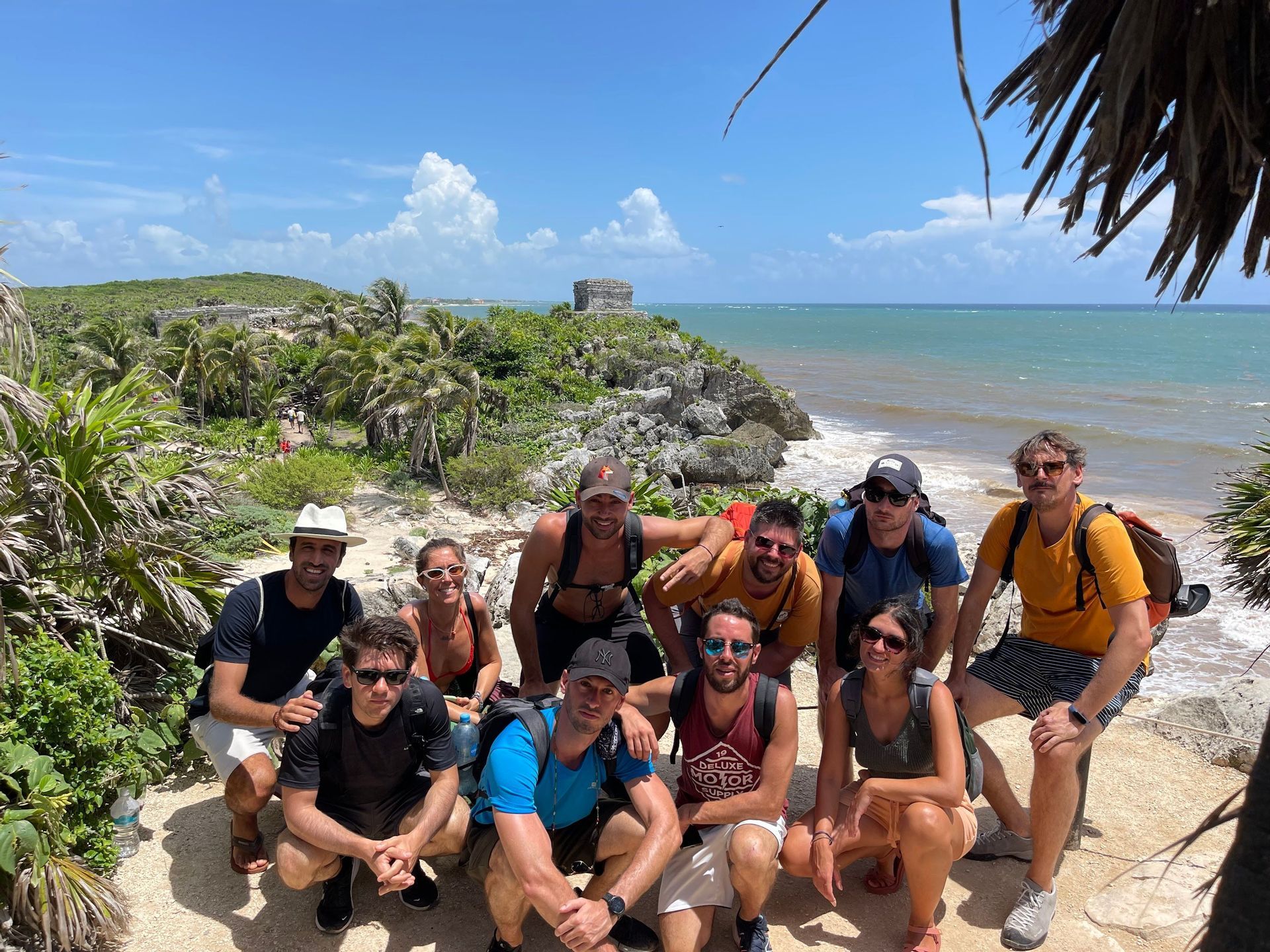 Un viaje en grupo de WeRoad posa para una foto en un acantilado costero con ruinas antiguas y el océano de fondo.