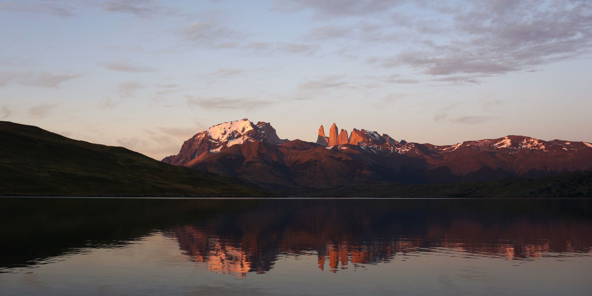 Vom Sonnenaufgang beleuchtete, gezackte, schneebedeckte Berge spiegeln sich im stillen See darunter.