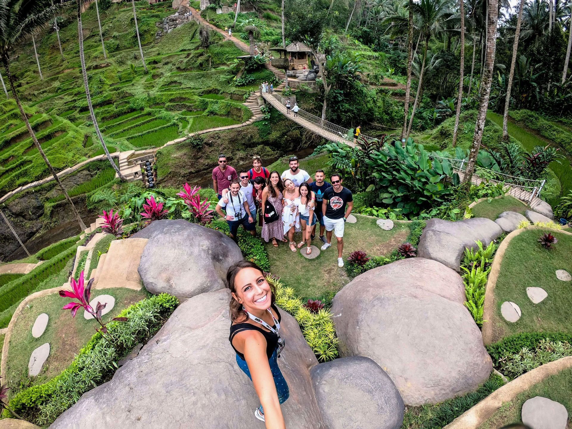 Una mujer se toma un selfie con su grupo de WeRoad, posando juntas en una colina con vistas a exuberantes terrazas de arroz verdes y palmeras.