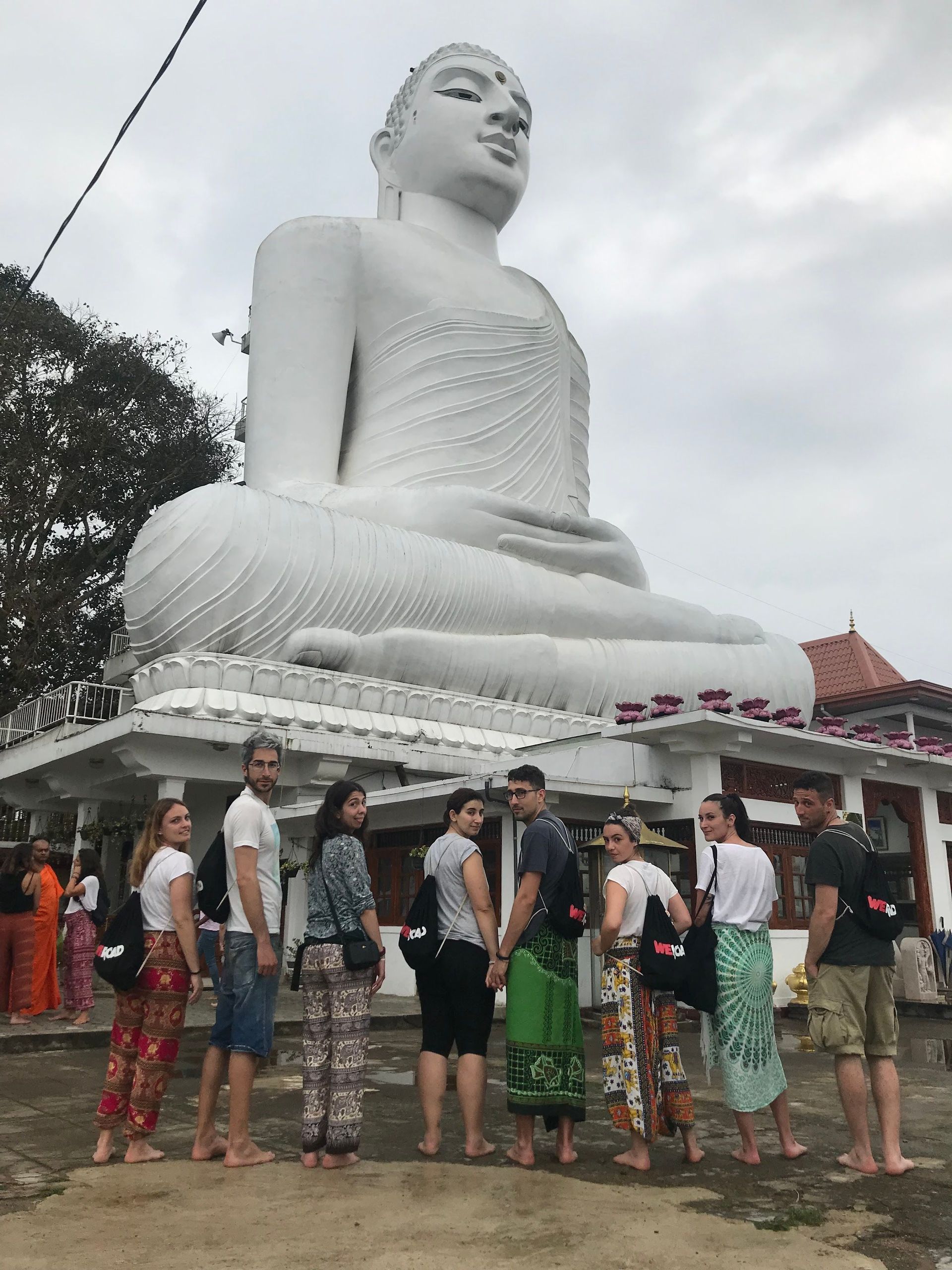 A WeRoad group trip stands barefoot looking at the camera in front of a giant white seated Buddha statue.