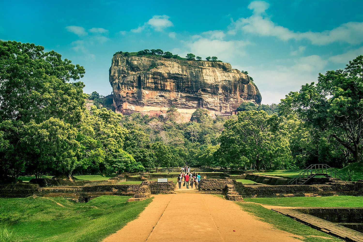 Un grupo de WeRoad recorre un sendero entre ruinas antiguas hacia una gran fortaleza rocosa rodeada de bosque.