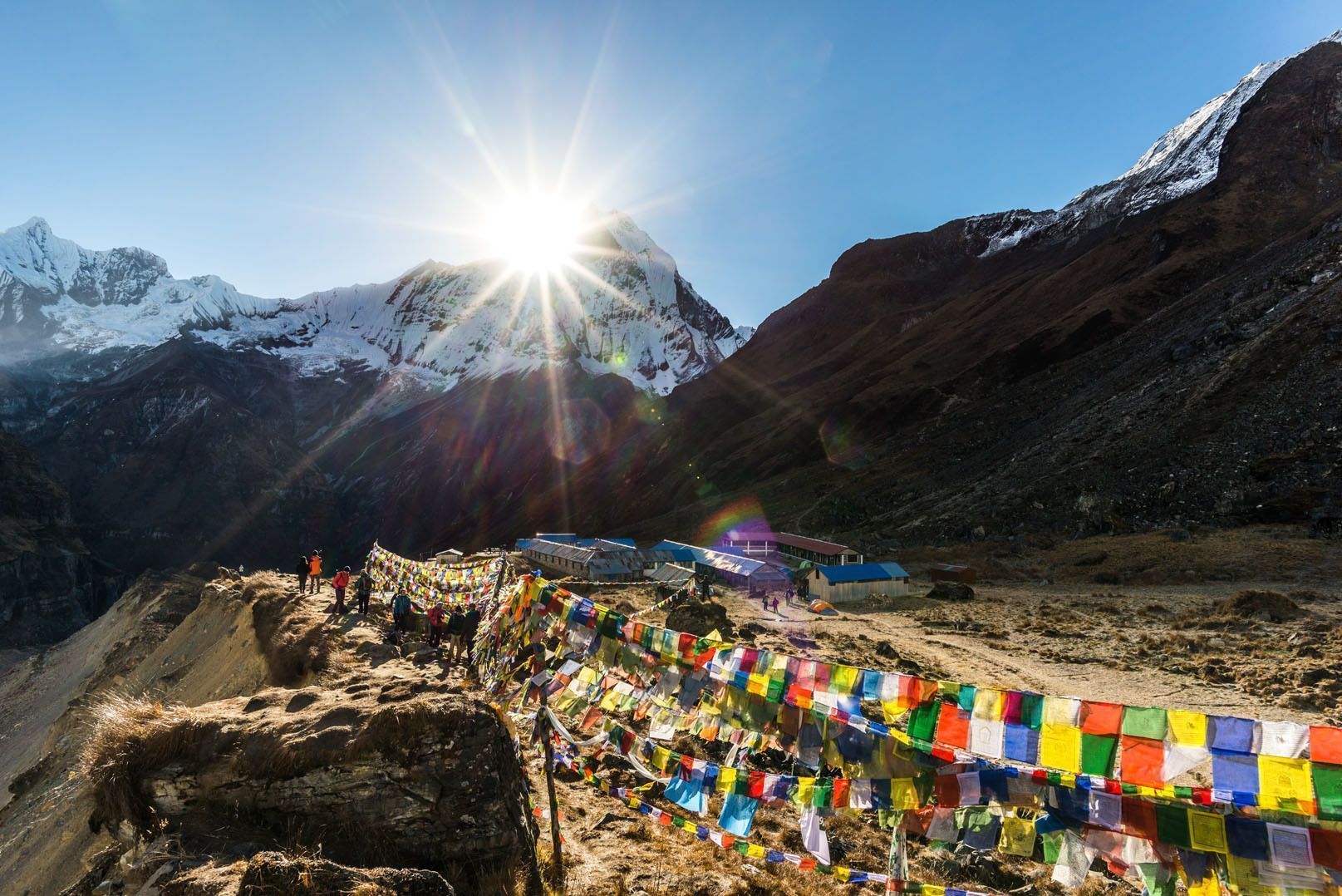 Un voyage de groupe WeRoad sur une crête de montagne ornée de drapeaux de prière colorés, surplombant des sommets enneigés sous un soleil éclatant.