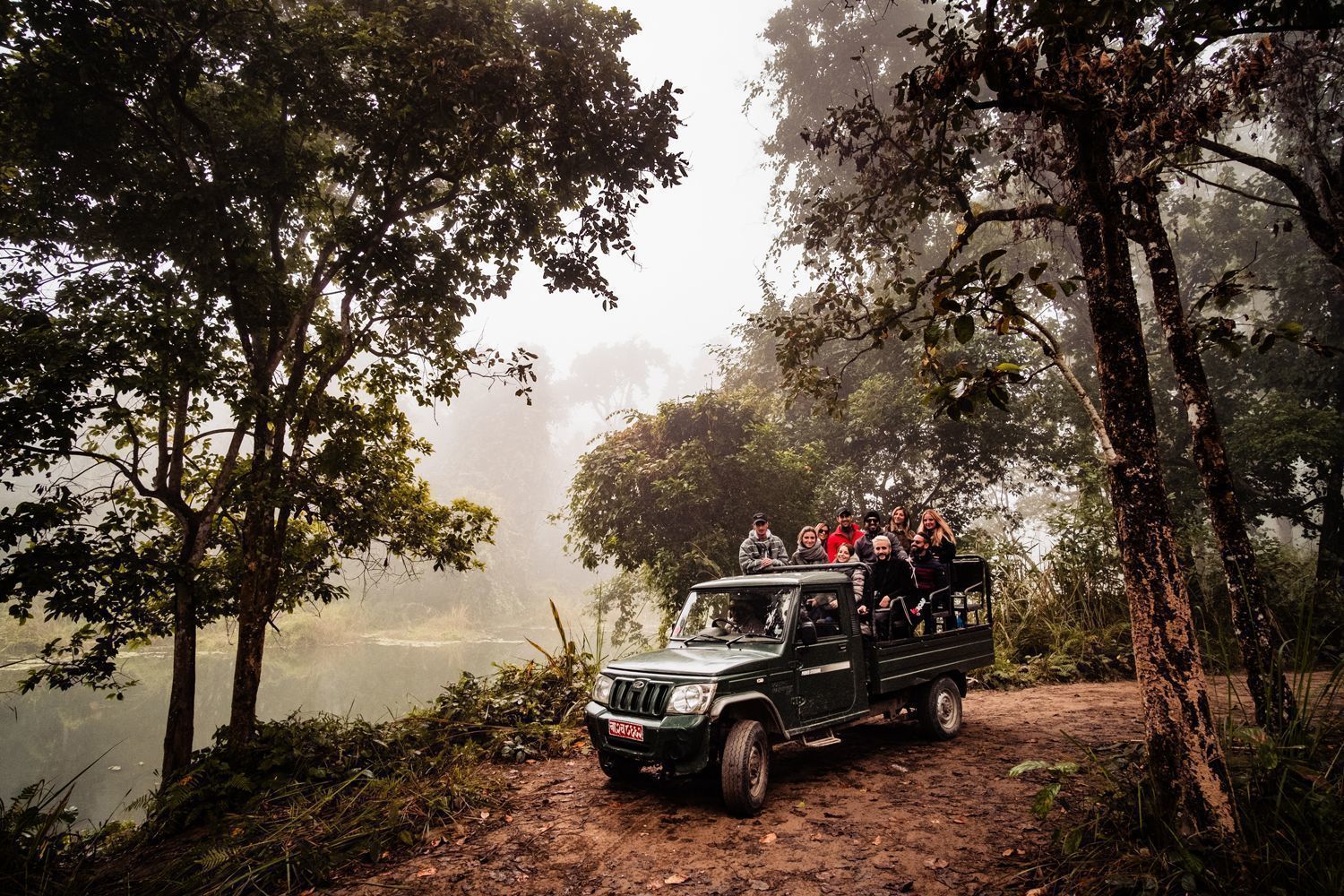 Un viaje en grupo de WeRoad en un jeep descapotable por un camino de tierra a través de un bosque con niebla junto a un río.