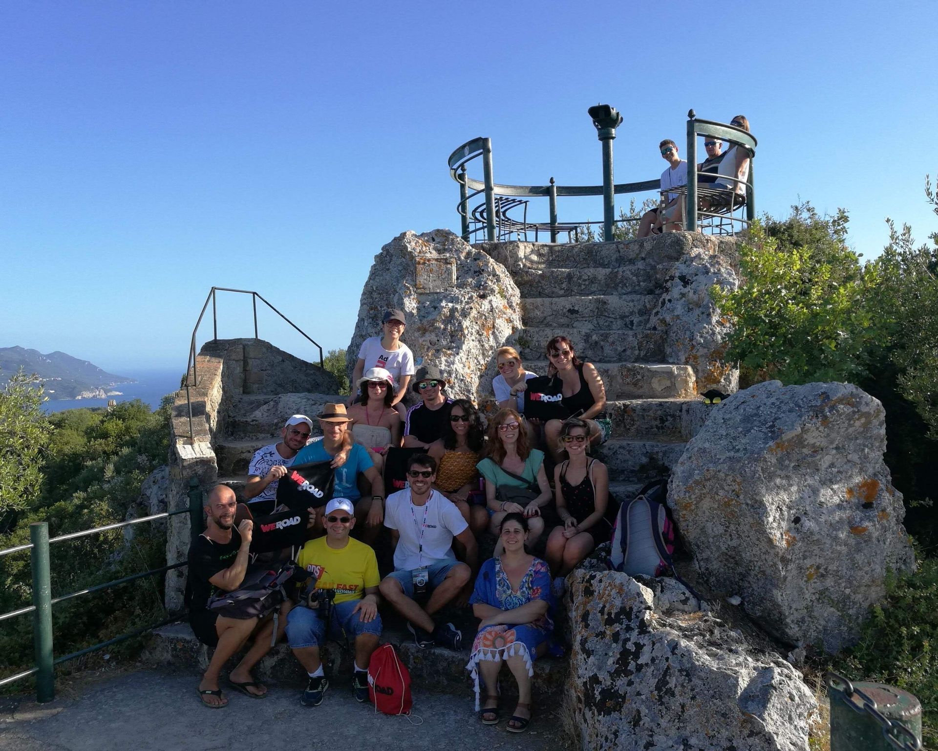 Un groupe WeRoad posant pour une photo sur des marches en pierre à un point de vue surplombant la mer et le littoral.