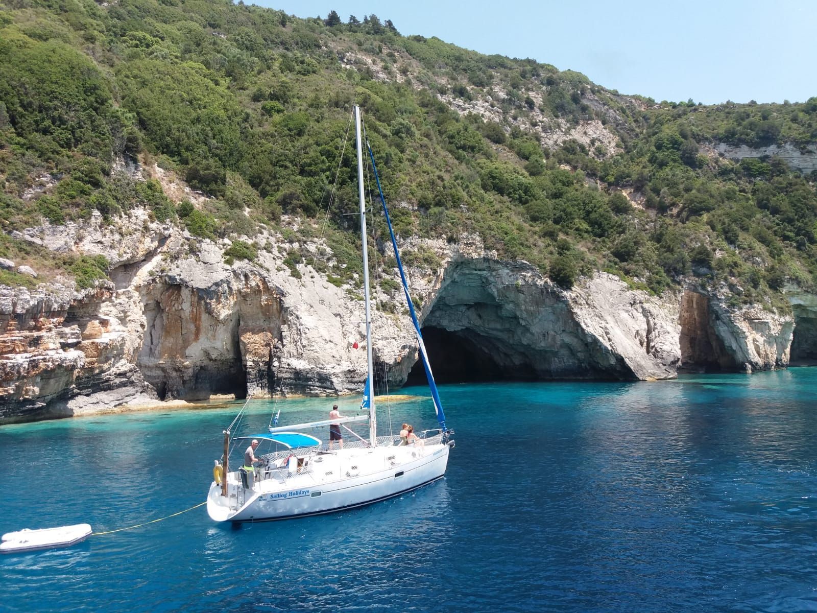 Un voyage de groupe WeRoad en voilier flotte sur des eaux turquoise calmes dans une crique avec des grottes marines et une falaise.