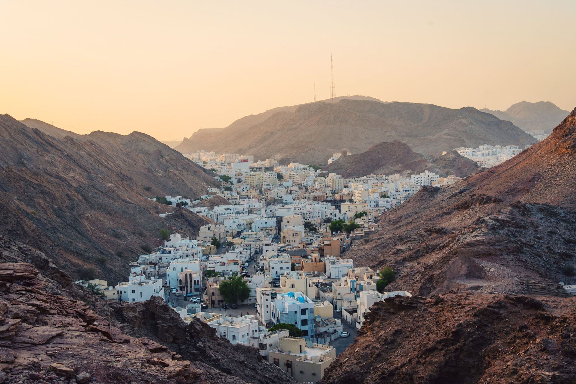 Una ciudad de edificios blancos anidada en un valle entre montañas escarpadas y rocosas durante un atardecer brumoso.