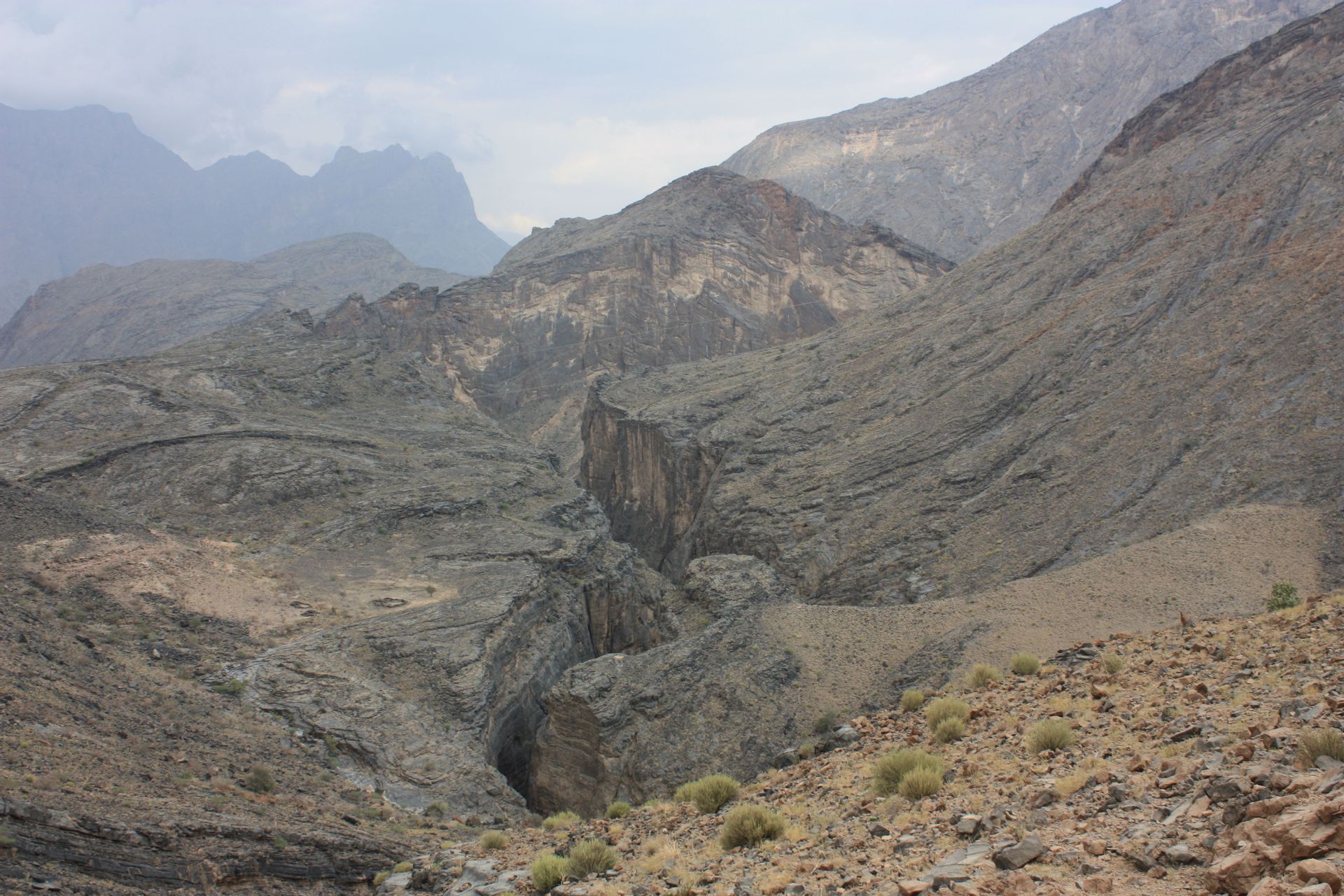 A vast and rocky mountain landscape with a deep canyon cutting through the center under an overcast sky.
