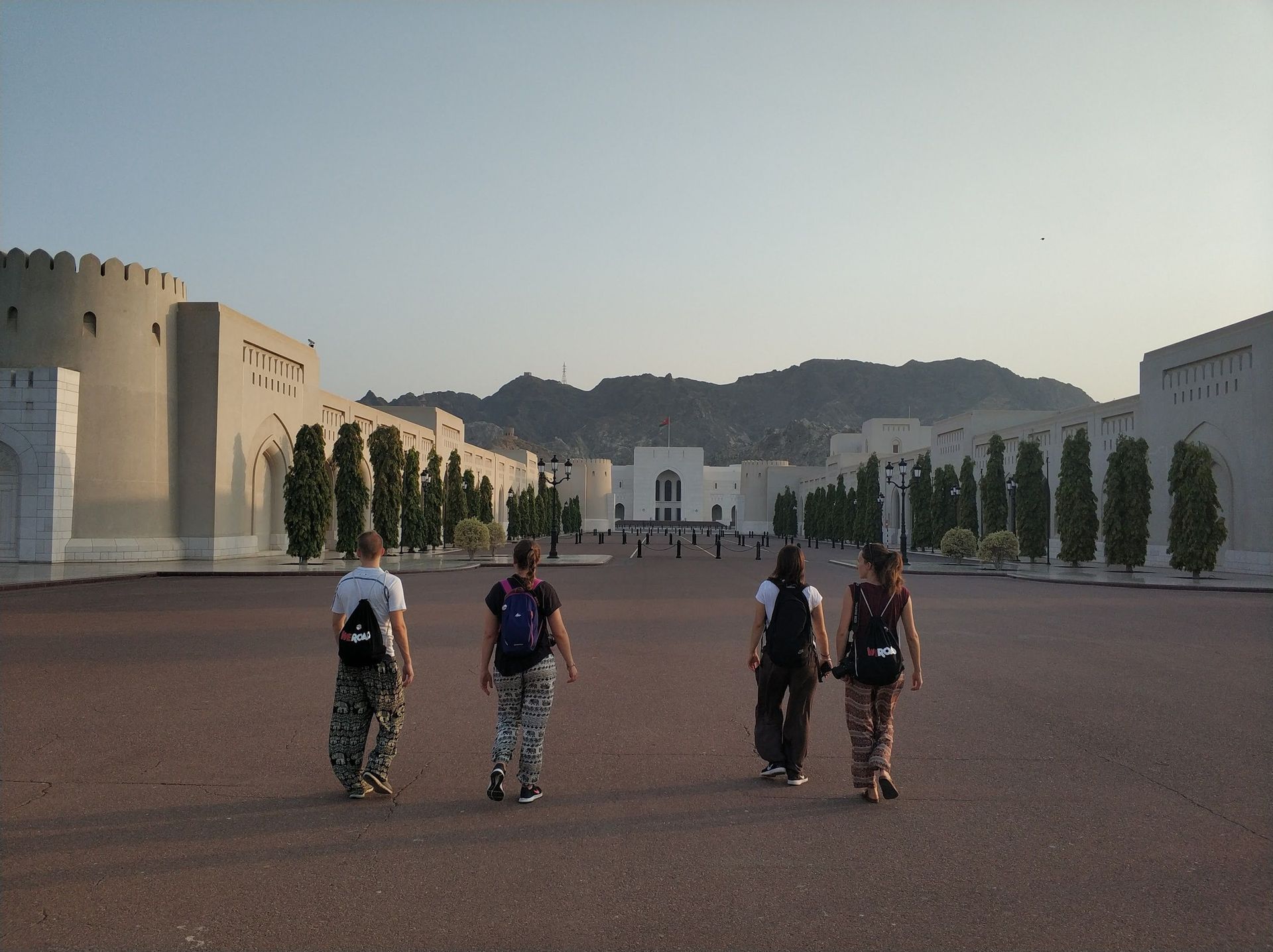 A WeRoad group trip walks across a large plaza towards a grand building with mountains in the background.