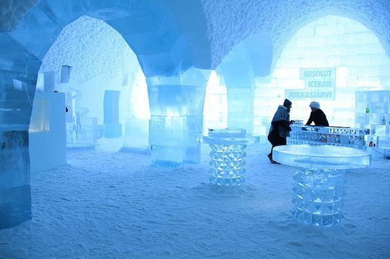 L'interno di un ice bar con soffitti ad arco, pilastri e tavoli scolpiti nel ghiaccio, con due persone al bancone.