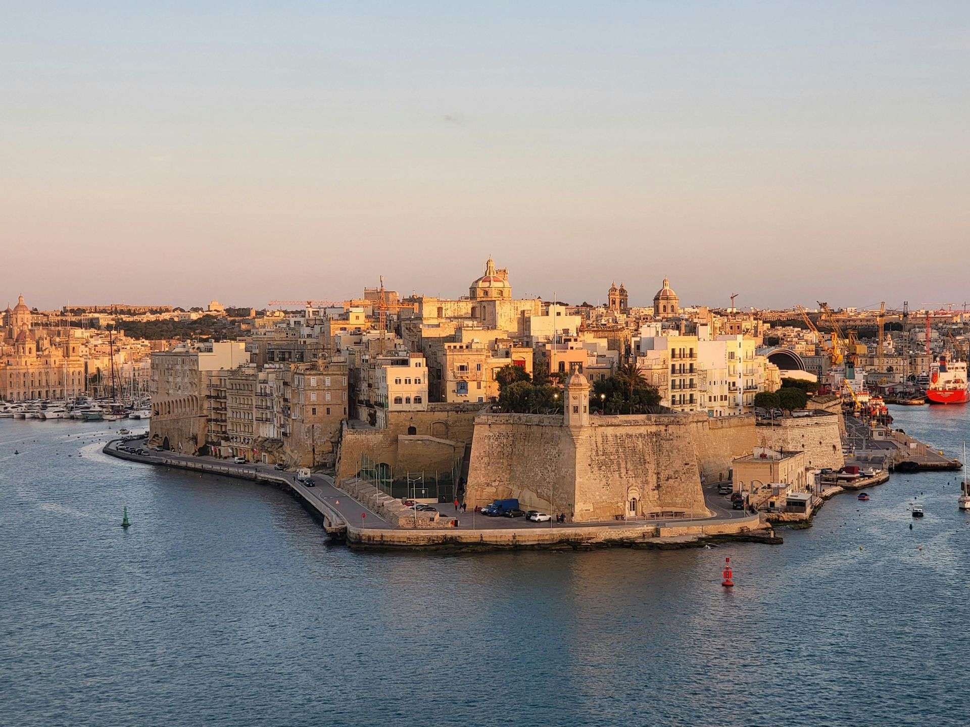 Una città storica fortificata su una penisola circondata dall'acqua, con i suoi edifici in pietra illuminati dal sole al tramonto.