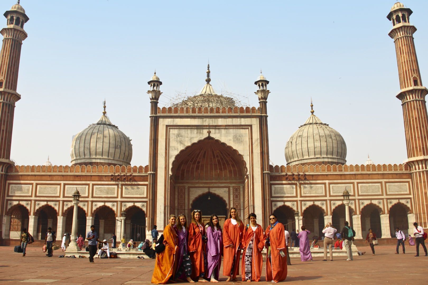 Un groupe WeRoad de femmes en robes colorées posent pour une photo devant une mosquée ornée de grands dômes.