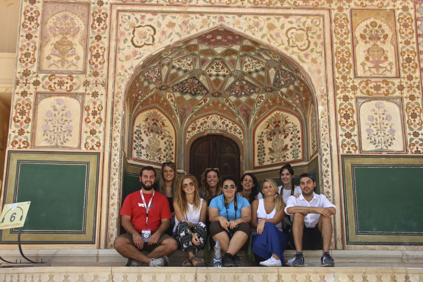 A WeRoad group trip posing for a photo on the steps of an ornate, arched building with intricate floral patterns.