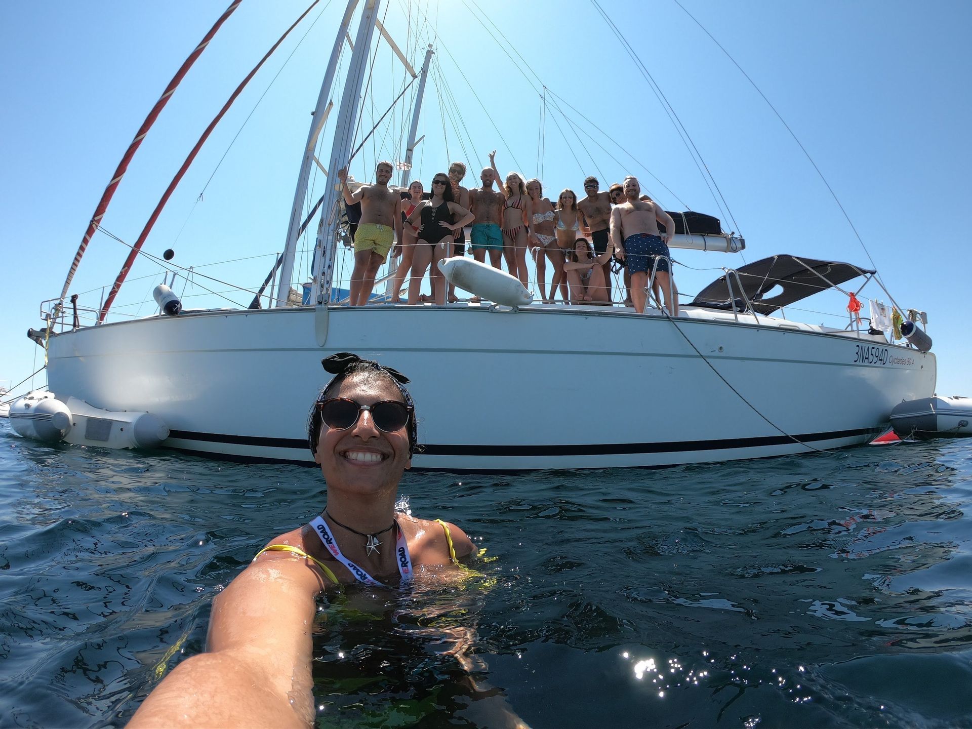 Eine lächelnde Frau macht ein Selfie aus dem Wasser, während eine WeRoad-Gruppenreise an Deck eines Segelbootes posiert.
