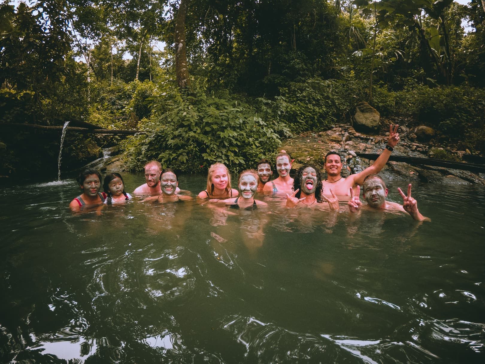 Eine WeRoad Gruppe lächelt mit Schlammmasken im Gesicht, während sie in einem Naturpool im Dschungel badet.
